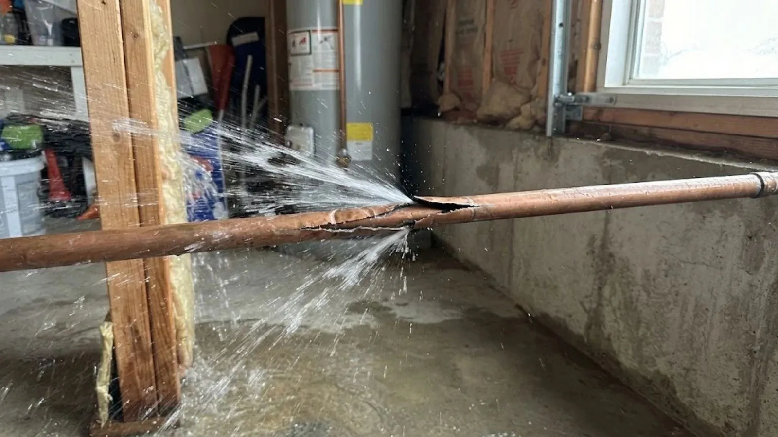 Burst copper pipe spraying water in a basement beside a water heater